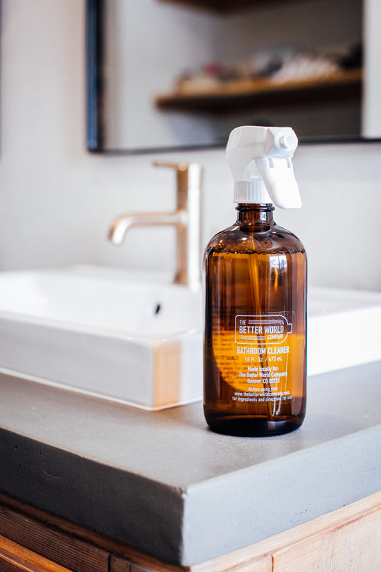 Bathroom Cleaner in a reusable amber glass foaming spray bottle on a bathroom vanity beside a sink.